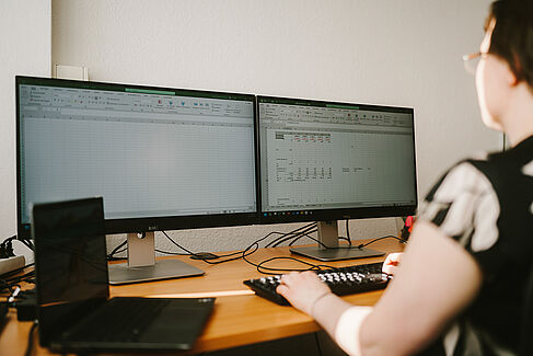 Katrin Dziergwa schaut auf einem Monitor, auf dem Excel geöffnet ist