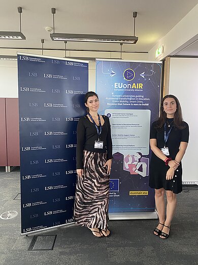 Zwei Frauen mit Namensschildern stehen vor Bannern mit den Logos von LSB und EUonAIR in einem Konferenzraum