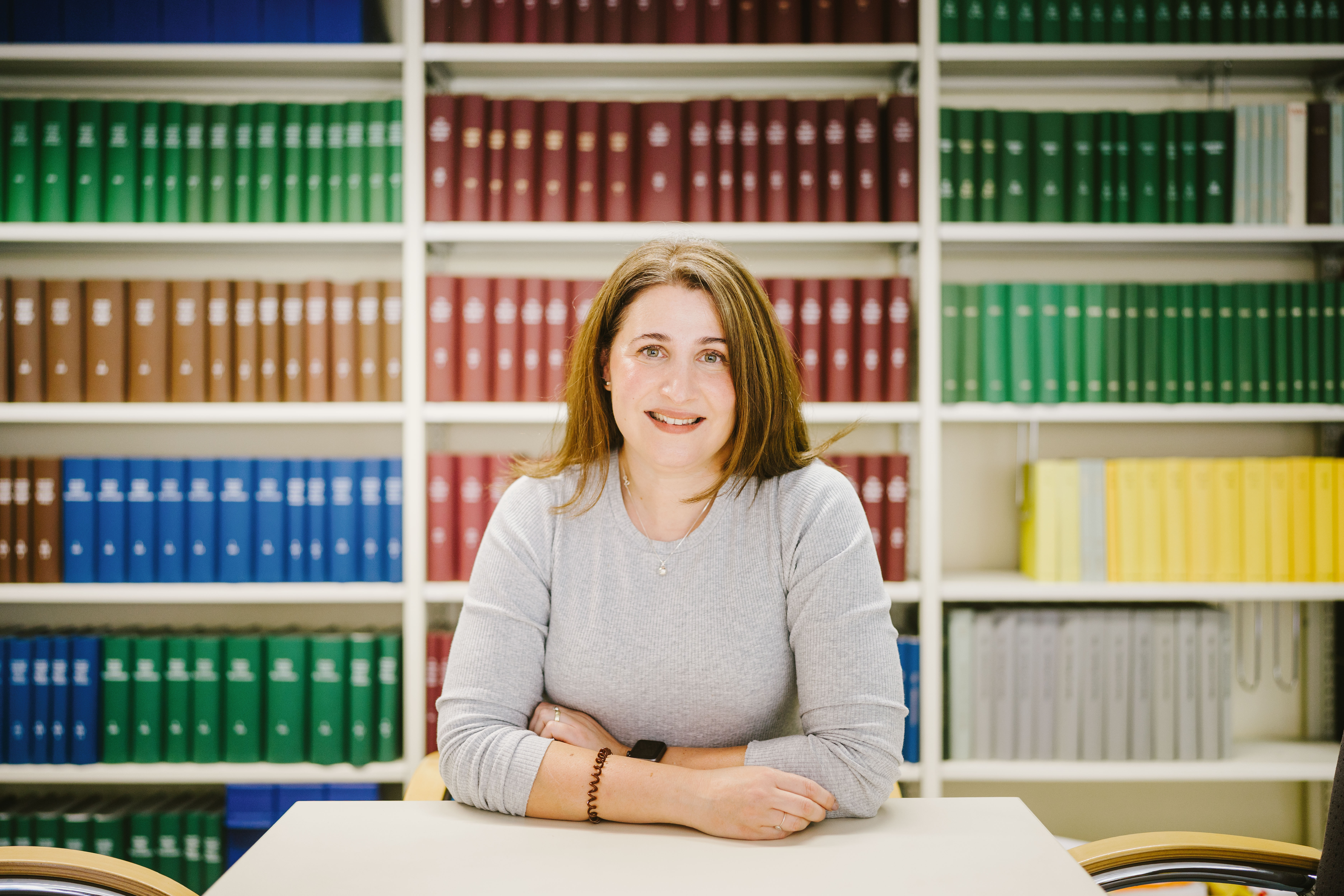 Evmorfia Conrad sitzt an einem Tisch vor einem Bücherregal