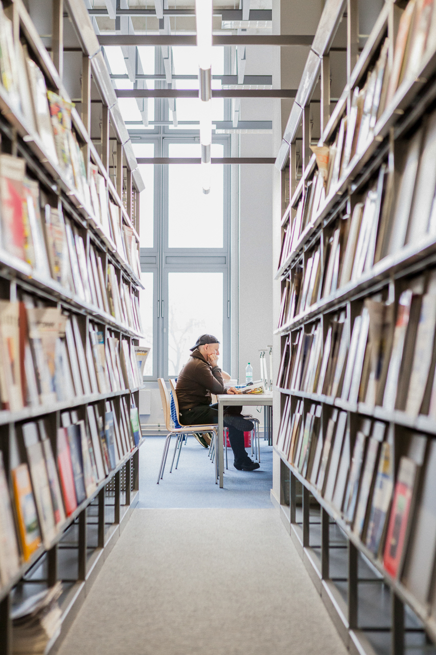 Student an einem Tisch, an beiden Seiten Zeitschriftenregale