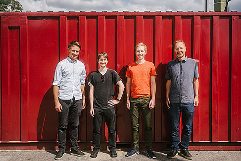 Vier Männer vor einem roten Container