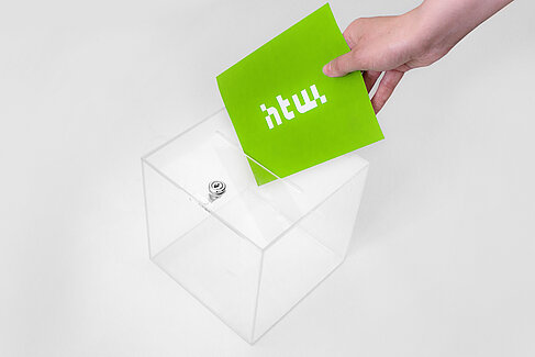 Transparente Wahlurne, ein Hand hält einen grünen Zettel mit HTW-Logo © HTW Berlin