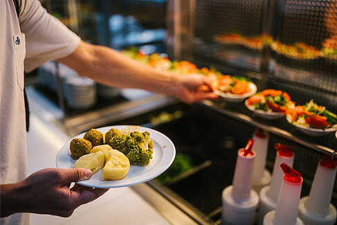 Hand mit Teller und Salatschüsseln