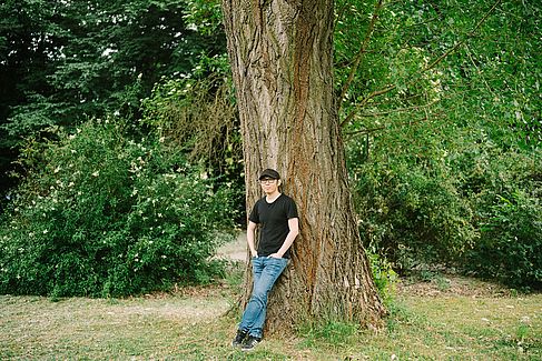 Niu Li lehnt an einem Baum auf dem Campus Treskowallee