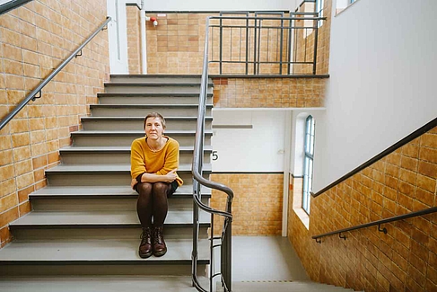 Suse Prejawa sitzt auf Stufen im Treppenhaus