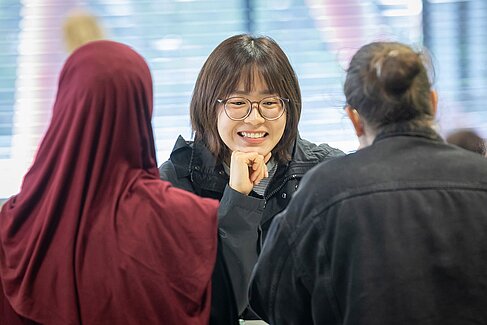Eine lachende Studentin, ihr gegenüber zwei andere Studierende von hinten