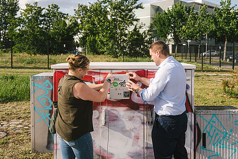 Zwei Projektmitarbeiter montieren einen Ultraschallsensor an einem Stromkasten.