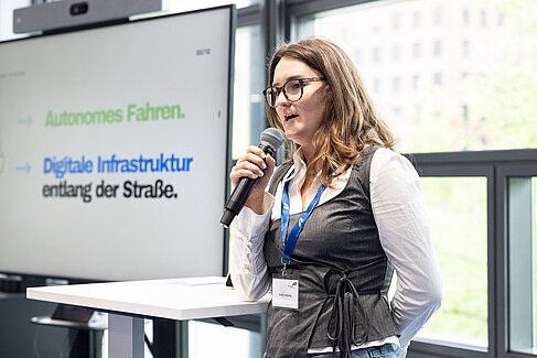 Studentin mit Mikrofon vor Bildschirm