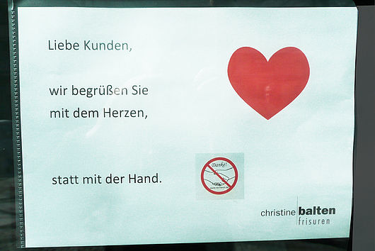 Zettel mit der Aufschrift "Liebe Kunden, wir begrüßen Sie mit dem Herzen statt mit der Hand."