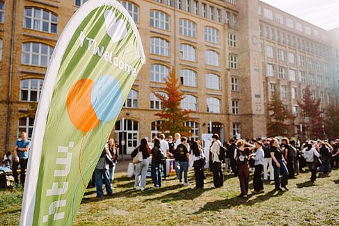 Beach-Flag "HTWelcome", im Hintergrund viele Menschen im Innenhof zwischen Gebäude C und B am Campus Wilhelminenhof bei der Erstsemesterbegrüßung © HTW Berlin/Alexander Rentsch