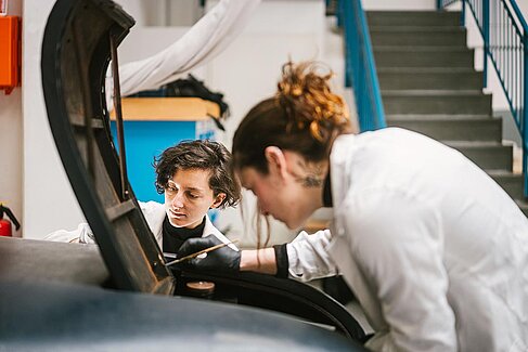 Frauen im weißen Kittel beugen sich über ein Auto.