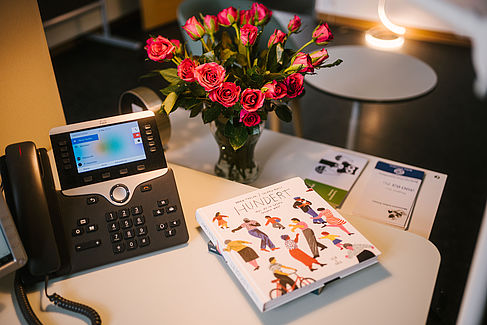 Schreibtisch mit Telefon, Blumen und einem Buch © HTW Berlin/Alexander Rentsch