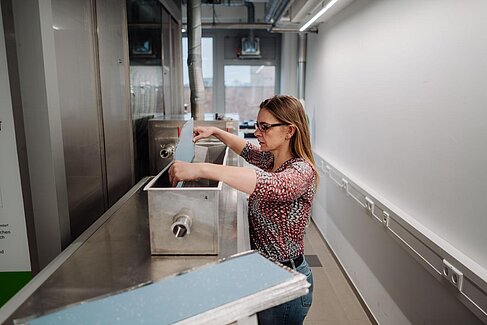 Simone Brandt platziert ein Bodenbelagsmuster in einer Edelstahlbox