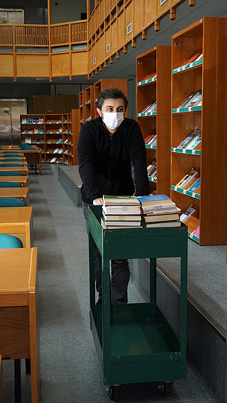 Mann schiebt Bücherwagen in einer Bibliothek