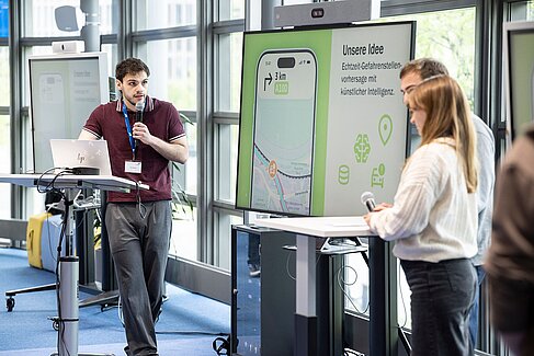 Studierende präsentieren vor einem großen Bildschirm