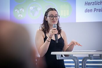 Studentin mit Mikrofin, im Hintergrund Jette Hausotter und ein Student