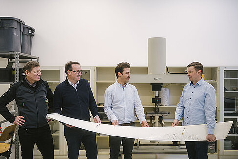Vier Männer halten ein Rotorblatt