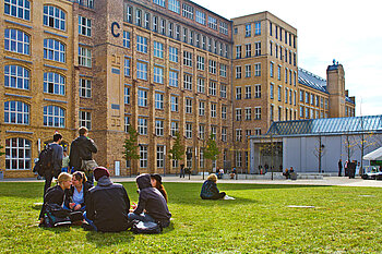 Studierende sitzen auf der Wiese im Innenhof vor Gebäude C am Erstsemestertag 