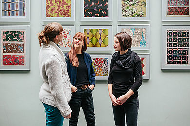 Drei Studentinnen vor einer Bilderwand