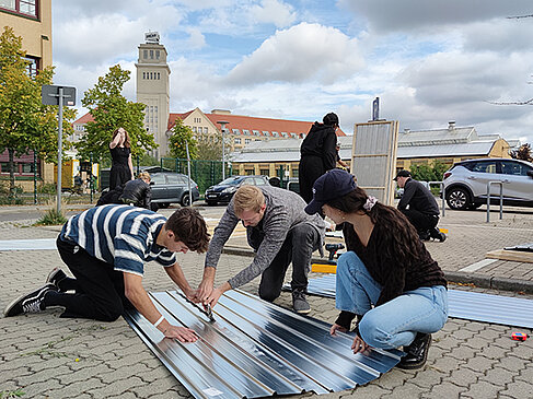 People kneel on the ground and cut corrugated iron