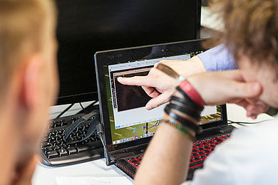 Informatik-Studierende zeigen auf einen Bildschirm