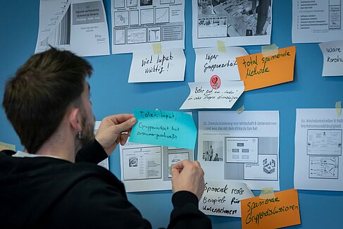 Studierender klebt Feedback Post It an eine Tafel
