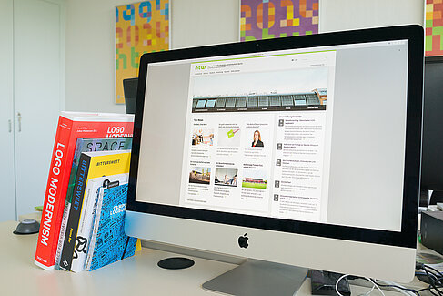 Bürschreibtisch mit Büchern und einem Bildschirm, auf dem die Webseite der HTW Berlin zu sehen ist.