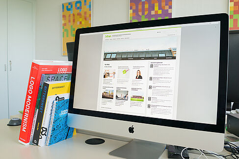 Bürschreibtisch mit Büchern und einem Bildschirm, auf dem die Webseite der HTW Berlin zu sehen ist.