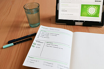 Arbeitsplatz mit Kalender, Wasserglas und Laptop