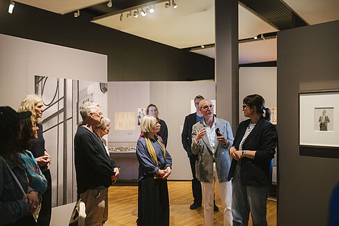 Mehrere Personen in einem Ausstellungsraum, eine Person erklärt etwas.