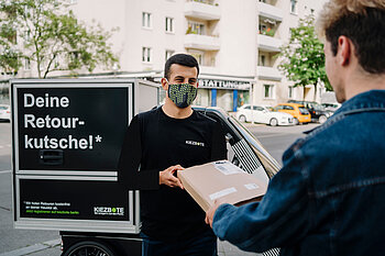 Ein Mann mit Maske übergibt ein Päckchen