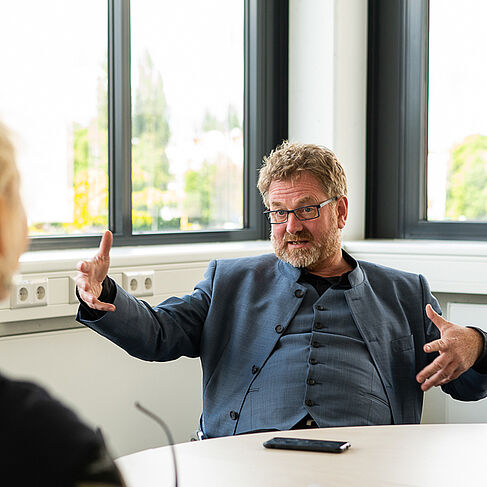 Carsten Busch sitzt an einem Tisch und gestikuliert mit den Armen