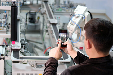 Mann mit Smartphone vor Maschine 
