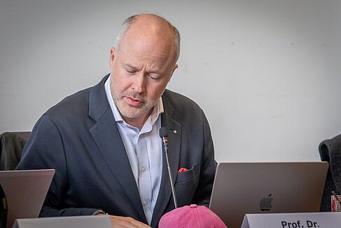 Kristoff Ritlewski sitzt an einem Tisch mit Mikrofon und blickt auf seine Unterlagen
