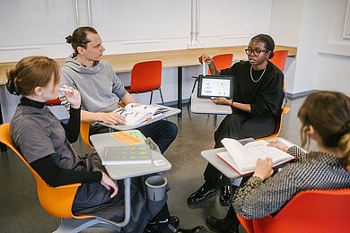 Lerngruppe sitzend auf flexibel angeordneten orangen und roten Stühlen mit Schreibflächen in einem neu gestalteten Seminarraum